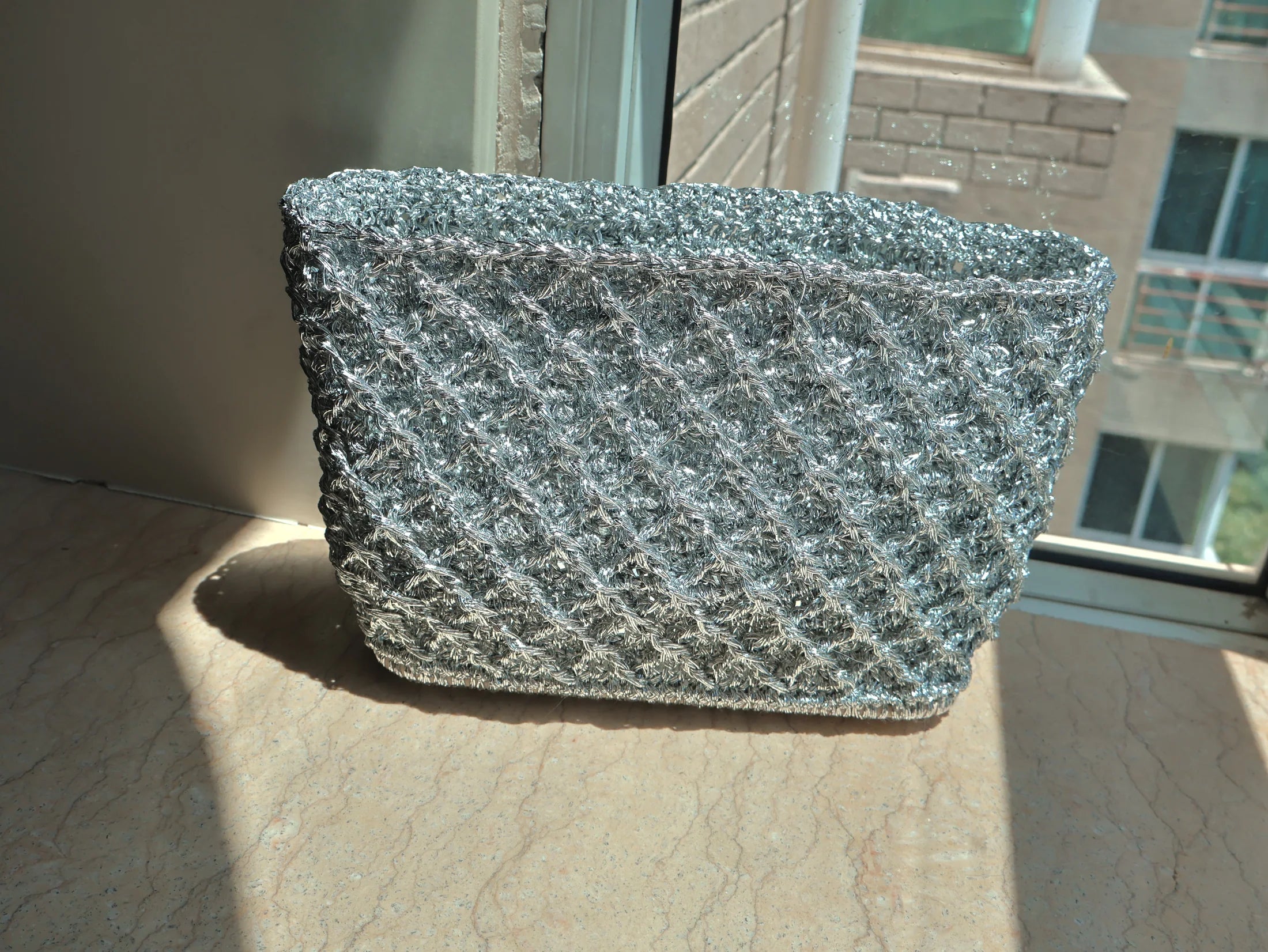 Silver hand-knitted bag casting a soft window shadow