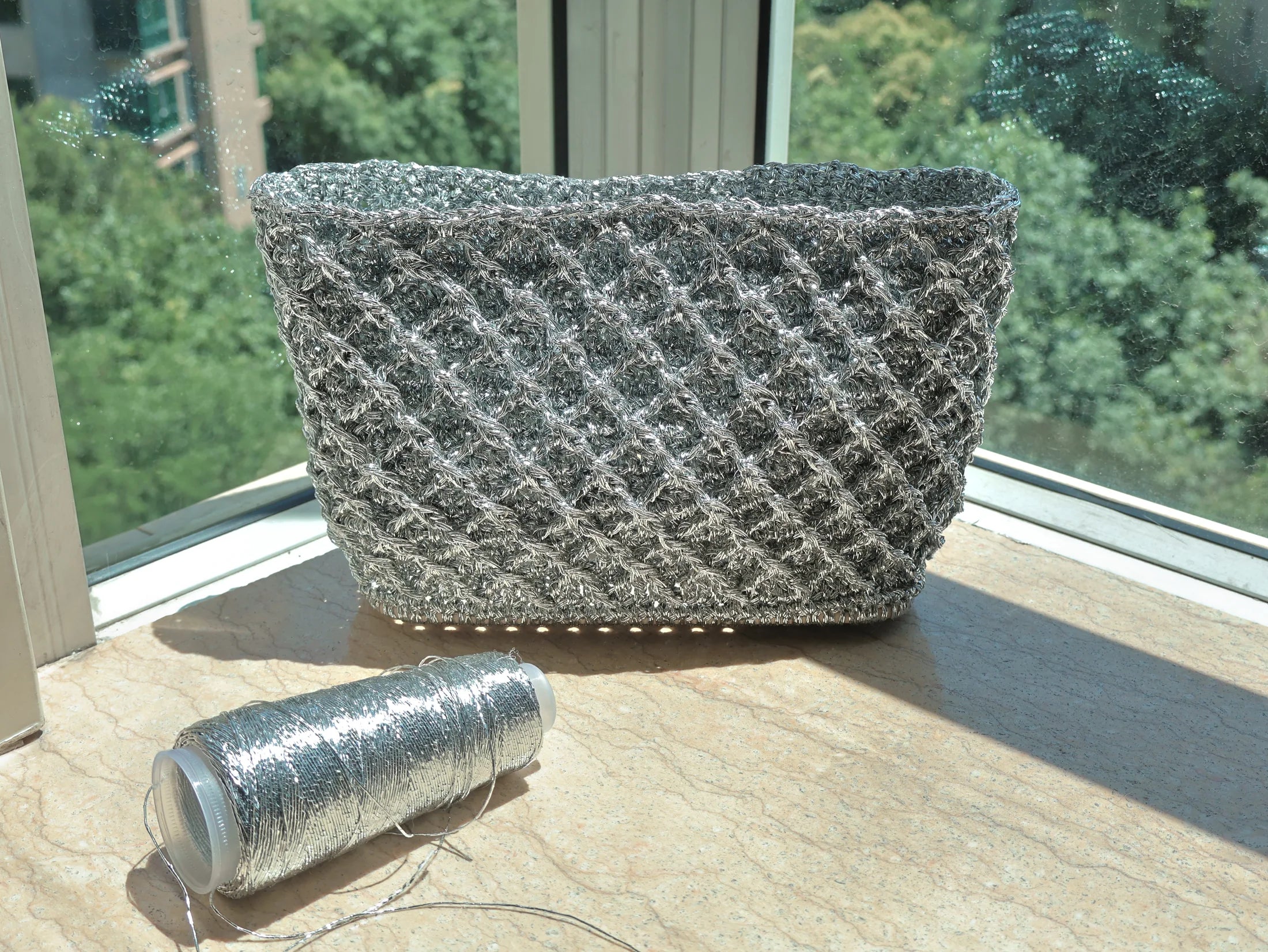 Silver hand-knitted bag beside its thread spool